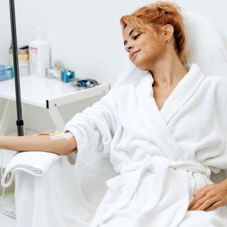 Portrait of woman sitting in armchair and closed eyes while receiving IV infusion with vitamins